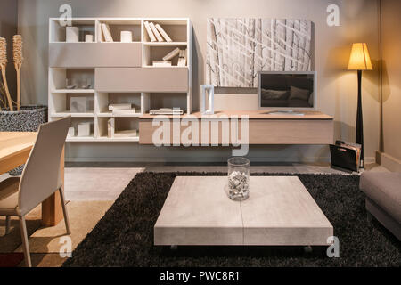Modern living room interior with dining table open plan to a lounge area with bookcase, television, coffee table and sofa illuminated by a standing co Stock Photo