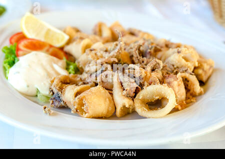 Serving of cooked calamari in batter on a plate with seafood tartare and fresh salad garnished with a slice of lemon. Stock Photo