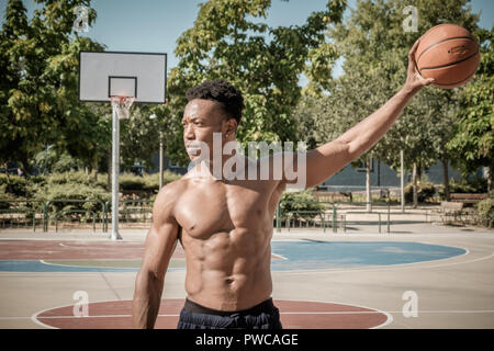 Close up of one afroamerican young man without tshirt playing basketball in a park in Madrid during summer at midday. He is standing and holding the b Stock Photo