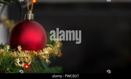Red bauble on a christmas tree decorated with sparkling tinsel with focus to small golden stars. Stock Photo