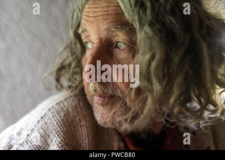Portrait of old man wit long gray hair and stubble looking sad, side view. Stock Photo