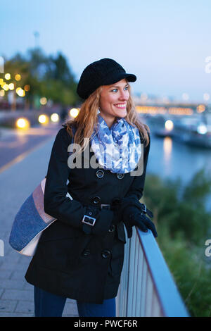 Happy young fashionable brunette caucasian woman in winter cap walking at evening in city Stock Photo
