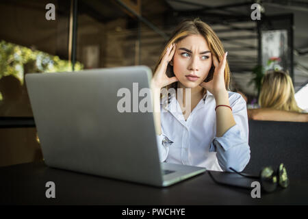 Stressed female student having headache touching temples preparing for test in cafe, frustrated millennial girl feels nervous or tired, afraid of exam Stock Photo
