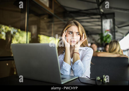 Stressed female student having headache touching temples preparing for test in cafe, frustrated millennial girl feels nervous or tired, afraid of exam Stock Photo