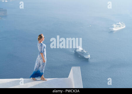 Happy woman in white and blue dress enjoying her holidays on Santorini, Greece. View on Caldera and Aegean sea from Imerovigli. Stock Photo