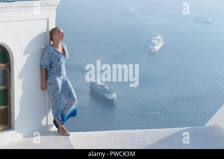 Happy woman in white and blue dress enjoying her holidays on Santorini, Greece. View on Caldera and Aegean sea from Imerovigli. Stock Photo