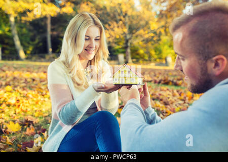 Young loving couple holding small model house in autumn garden or park. Stock Photo