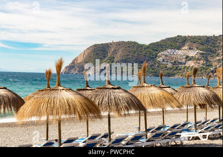 Mediterranean coastline in the summer time. The beach in Southern Spain (La Herradura, Alumnecar, Province of Granada) lined with straw umbrellas. Stock Photo