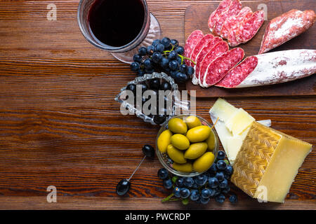 Platter with sliced Italian hard cheese pecorino toscano, homemade dried meat salami, glass of red wine, grape, olives on wooden board, snack bar Stock Photo