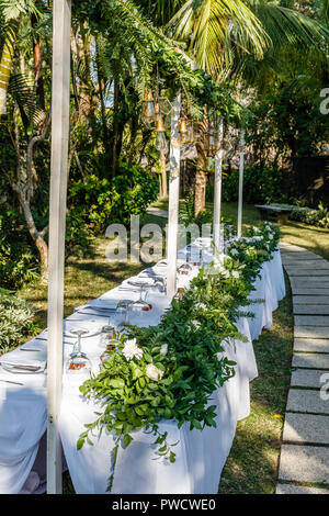 Set table for a wedding dinner decorated with flowers and glass lamps. Concept of a tropical wedding. Vertical image. Stock Photo