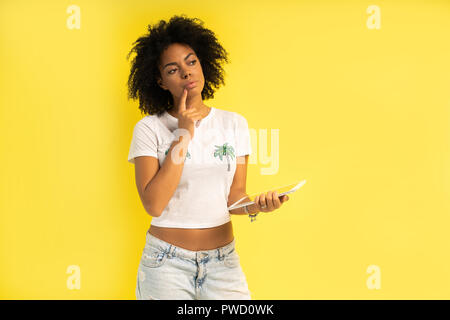 Pretty young afro american woman standing and using tablet computer isolated over yellow background. Stock Photo