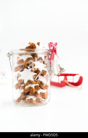 Zimtsterne, German Christmas cookies in a glass jar with Christmas decoration and a red sledge in the background. Shallow depth of field. Low angle vi Stock Photo