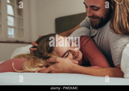 Smiling woman with eyes closed enjoying the love and care of her husband. Smiling man lying on bed with his wife holding hands and loving her. Stock Photo