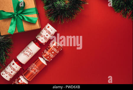 Beautiful flay lay of christmas crackers with gift box and garland on red background. Christmas flat lay design with copy space. Stock Photo