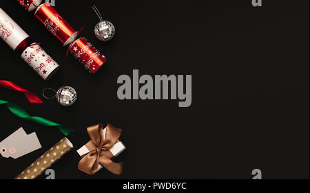 Christmas decoration flat lay on black background. Directly above shot of christmas crackers, mirror balls, colorful ribbons, tags and gift box with c Stock Photo