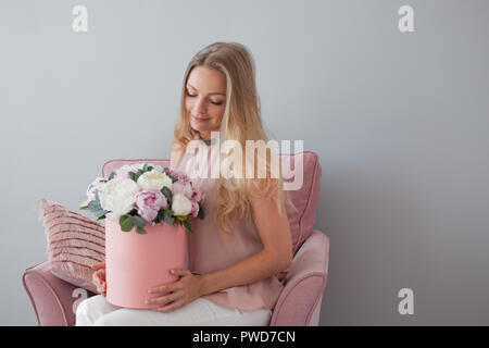 Happy blonde woman with flowers in a hat box. Bouquet of peonies. Girl in a soft pink dress with a pink bouquet of peonies Stock Photo