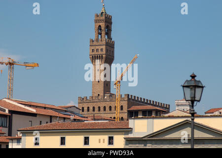 The tower of the Palazzo Vecchio against a bright blue summer sky with building cranes in the foreground. Stock Photo