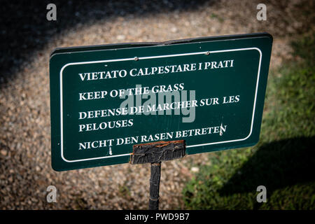 A green sign that reads 'Keep off the grass' in four languages on the grounds of the Pitti Palace in Florence, Italy. Stock Photo