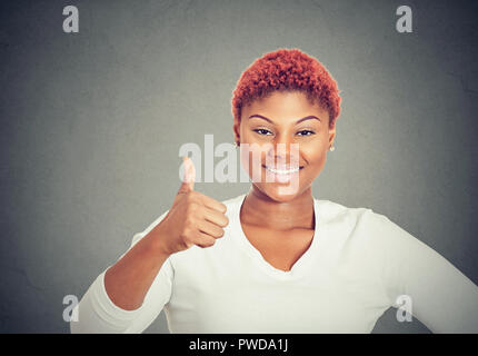 Happy young woman holding thumb up and smiling at camera on gray background Stock Photo