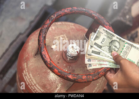 In Indian Gas price reach beyond capacity of poor people, Indian man holding Indian currency and LPG gas cylinder and waiting in queue to exchange emp Stock Photo