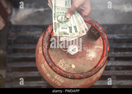 In Indian Gas price reach beyond capacity of poor people, Indian man holding Indian currency and LPG gas cylinder and waiting in queue to exchange emp Stock Photo