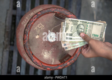 In Indian Gas price reach beyond capacity of poor people, Indian man holding Indian currency and LPG gas cylinder and waiting in queue to exchange emp Stock Photo