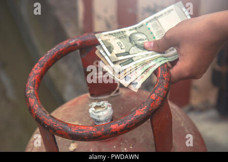 In Indian Gas price reach beyond capacity of poor people, Indian man holding Indian currency and LPG gas cylinder and waiting in queue to exchange emp Stock Photo