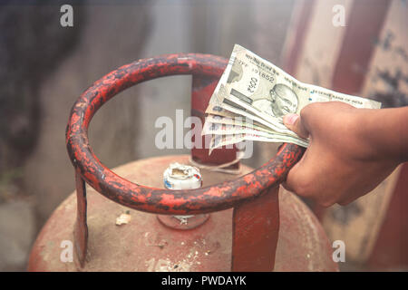 In Indian Gas price reach beyond capacity of poor people, Indian man holding Indian currency and LPG gas cylinder and waiting in queue to exchange emp Stock Photo