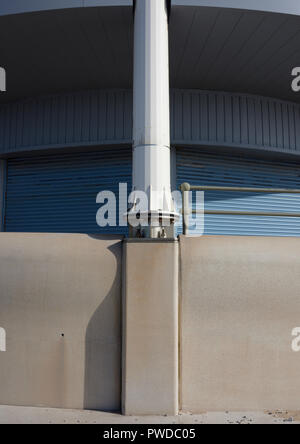 Wind turbine mast mounted on concrete sea wall with curved shuttered buiding behind in Cleveleys on the fylde coast in lancashire uk Stock Photo