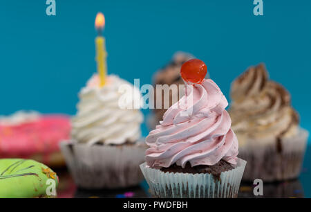 Chocolate muffin or cupcake with cherry perched on top of a twirl of pink icing backed by other assorted cakes Stock Photo