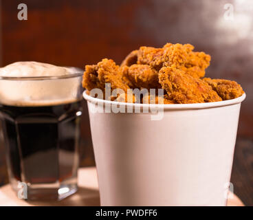 Tub of fried crumbed chicken pieces with beer served for a pub lunch or takeaway in a close up side view Stock Photo