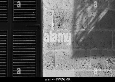 Wooden Shutter and strong shadow cast on stone wall Ciutadella Menorca Spain Stock Photo