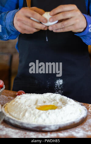 Male chef is breaking eggs into flour on wooden table. Stock Photo