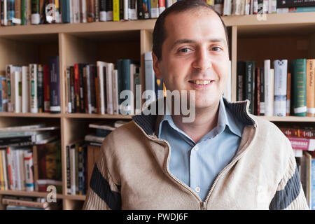 a smiling man in a jumper a blue shirt in a library Stock Photo