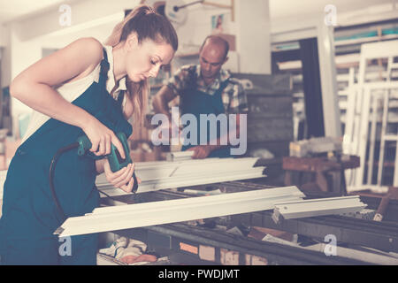 Young female using electric drill on window frame at factory Stock Photo