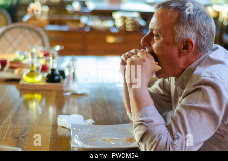 The Man with pleasure bites an appetizing burger in a steak house restaurant. Stock Photo