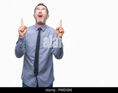 Middle age hoary senior business man wearing glasses over isolated background amazed and surprised looking up and pointing with fingers and raised arm Stock Photo