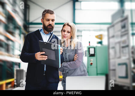 A portrait of a serious mature industrial man and woman engineer with laptop in a factory, working. Stock Photo