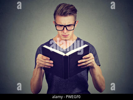 Young man in glasses looking confused while trying to read smart book on gray background Stock Photo