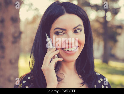 Beautiful ethnic woman having phone call while smiling and standing outdoors looking away Stock Photo