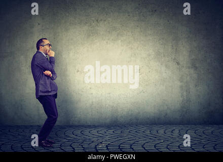 Side view of anxious businessman in fear standing nervously on gray background looking away Stock Photo