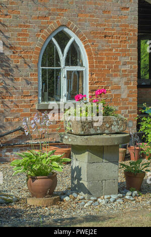 ​Various Plant containers in front of a cottage wall. Pointed arched window circa 1830. Ingham. Rural Norfolk. Long and short brickwork with bricks made from local clay; stone impurities causing some ​erosion. Stock Photo