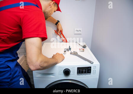 plumber installing washing machine in domestic bathroom Stock Photo