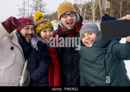 Waist up portrait of four happy young people taking selfie photo while having fun outdoors in winter Stock Photo