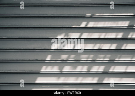 Gray metal roller shutter door with shadows pattern. Background photo texture, front view Stock Photo