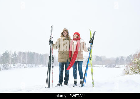 Full length portrait of loving young couple embracing and smiling happily while taking break during skiing trip and posing against beautiful winter la Stock Photo