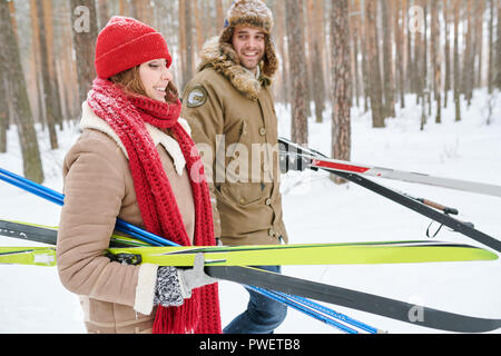 Side view portrait of active young couple carrying skis chatting on the way back in beautiful winter forest, copy space Stock Photo