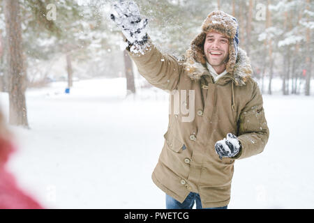 Waist up portrait of handsome young man enjoying snowball fight with friends in beautiful winter forest, copy space Stock Photo