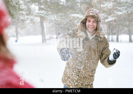 Waist up portrait of handsome young man laughing happily while enjoying snowball fight with friends in beautiful winter forest, copy space Stock Photo