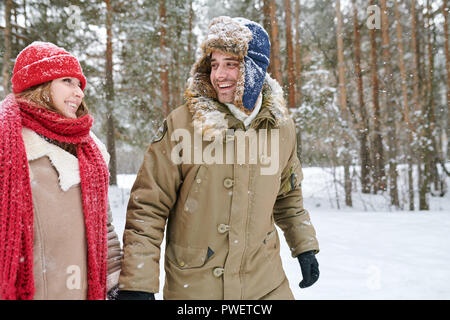 Waist up portrait of handsome young man looking at girlfriend and smiling happily while walking together through beautiful winter park, copy space Stock Photo